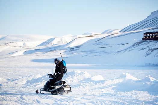 A man on a snowmobile with a gun and shovel for safety