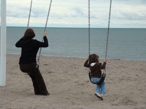 this mother and daughter are swinging as they watch the water