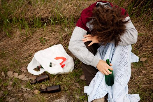 A drunk person sitting in a ditch with a wine bottle