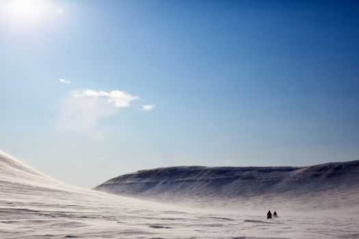 A barren winter landscape with two snowmobiles travelling accross the horizon