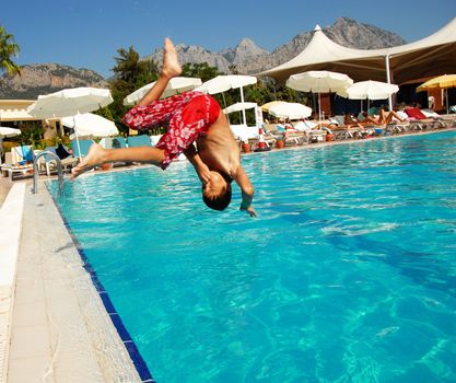 boy jumping into blue swimming pool in resort
