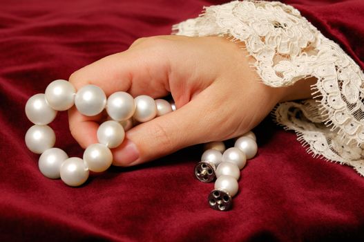 Female hand holding a  necklace from natural pearls on a red velvet surface