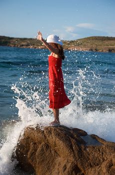 Pretty girl splashing by the wave on the beach at sunset time