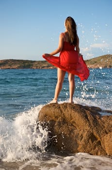 Pretty girl splashing by the wave on the beach at sunset time