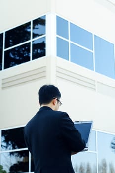 A businessman working on his laptop outside his office buildings