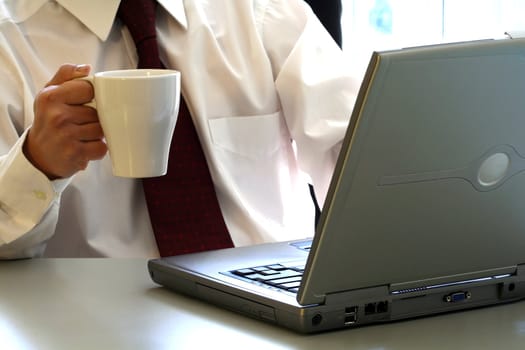 A businessman is drinking a cup of coffee and working on his laptop