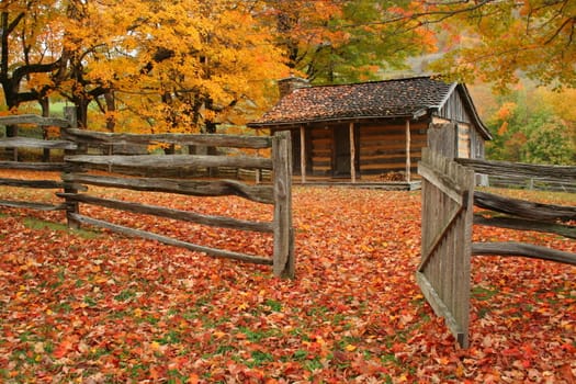 Old cabin during fall of the year with wooden fence and an open gate.
