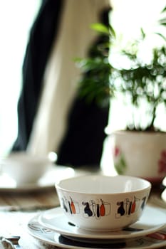 An interior shot of a restaurant showing a bowl, a plate and a waiter in background