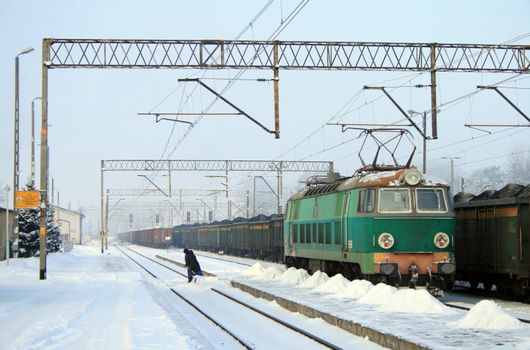 Freight train with the electric locomotive and woman taking care of the snow at the railway station
