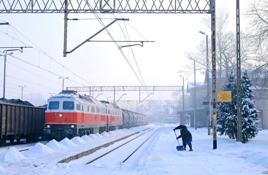 Freight train with the diesel locomotives and woman taking care of the snow at the railway station

