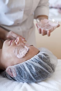 Beautician applying facial mask as part of cosmetic procedure