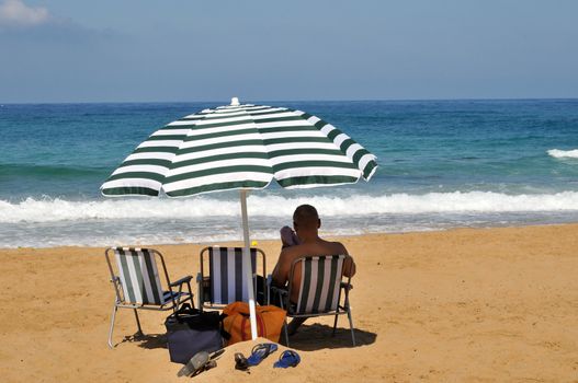 man sits on a chair under an umbrella on the beach
