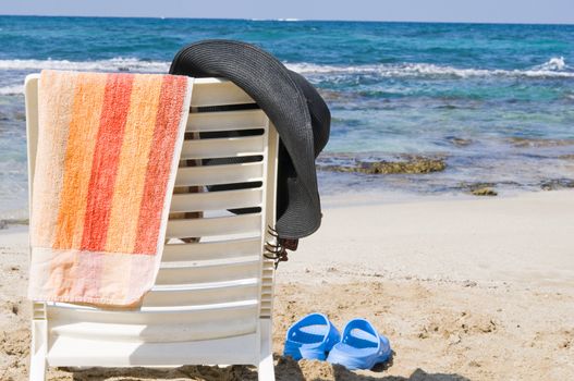 
A hat, a towel hanging on a chair on the beach by the sea