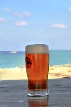 
	
A glass of beer is on the table in a pub on the beach