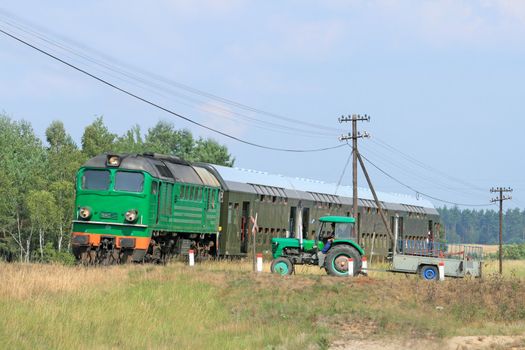 Passenger train passing the railroad crossing with a tractor

