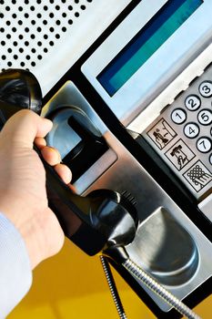 Picture of a male hand retrieving the handset of a public telephone in order to make a call