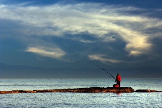 Picture of a lone fisherman on a thin strip of rock
