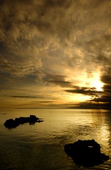 Spectacular golden sunset over silhouetted sea rocks. Room for text on top.