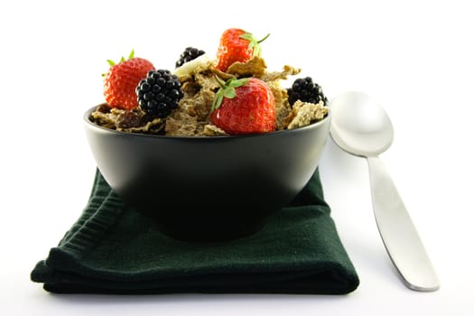 Crunchy looking delicious bran flakes and juicy fruit in a black bowl with a spoon on a black napkin on a white background