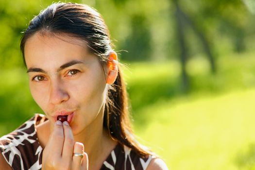 A young woman eating a handful of cherries outdoors