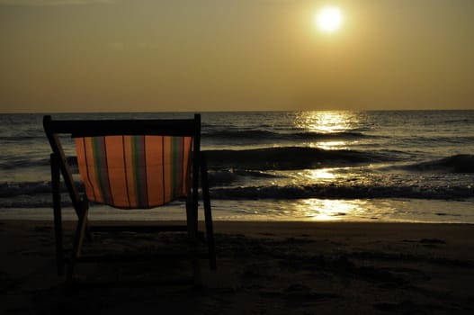 A lone beach chair as the sun sets over the ocean in Asia
