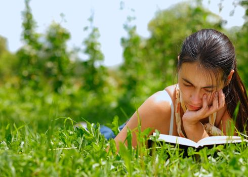 Young attractive woman reading a book lying on a grass