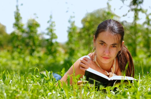 Young attractive woman reading a book and lying on a grass