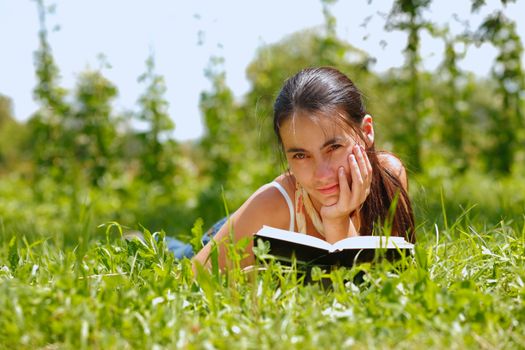 Young attractive woman reading a book and lying on a grass