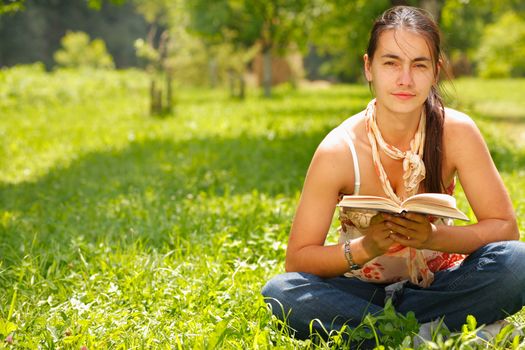 Young attractive woman reading a book and sitting on a grass