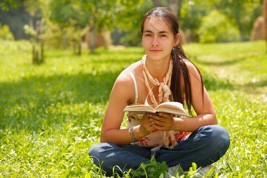 Young attractive woman reading a book and sitting on a grass