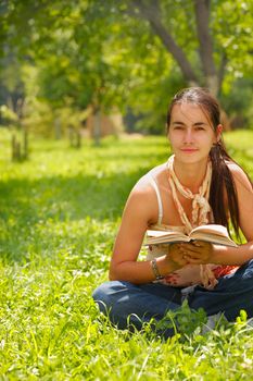 Young attractive woman reading a book and sitting on a grass