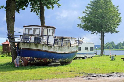 Old vintage boat standing on the grass near the lake
