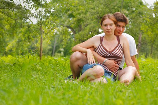 Young attractive couple sitting on a grass in a meadow