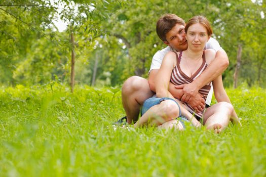 Young attractive couple sitting on a grass in a meadow