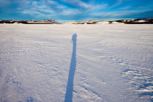 Long mid-winter shadow of person hiking through snowy landscape.