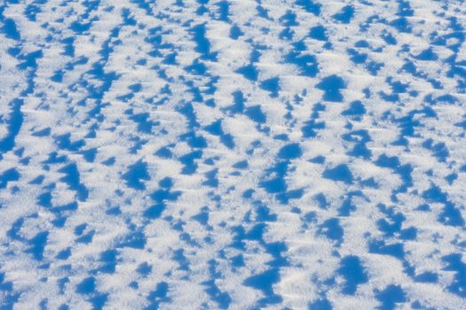 Windblown snow surface in bright sun, background texture pattern.