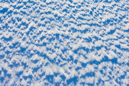 Windblown snow surface in bright sun, background texture pattern.