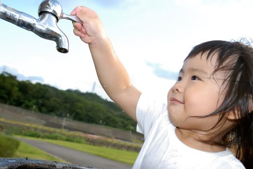 She is a happy baby washing her hand and turn off faucet in the outdoor.