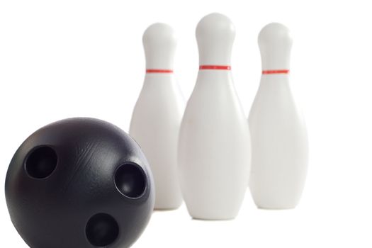 A plastic bowling ball rolling towards three pins, isolated against a white background