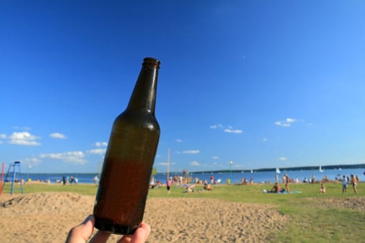 Bottle of beer against the beach, lake and blue sky
