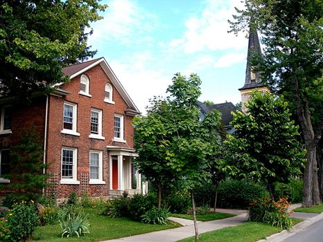 Red brick house surrounded by a lot of green vegetation and pavement