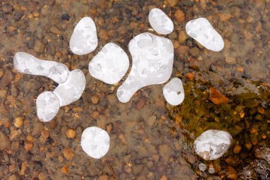 Air bubbles and cracks in thick layer of crystal clear ice over gravel bottom.