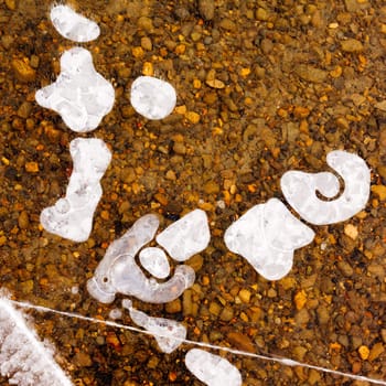 Air bubbles and cracks in thick layer of crystal clear ice over gravel bottom.