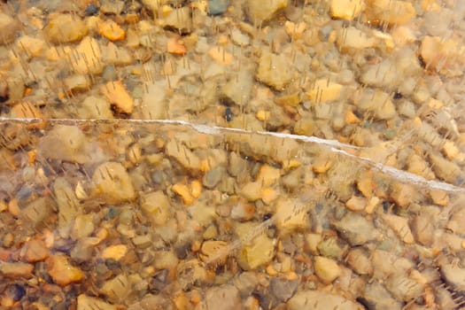 Air bubbles and cracks in thick layer of crystal clear ice over gravel bottom.