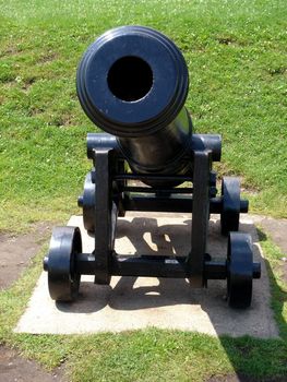 Black cannon on four wheels viewed from the front surrounded by green grass