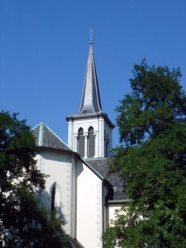 Bell-tower of white protestant church behind trees by beautiful weather