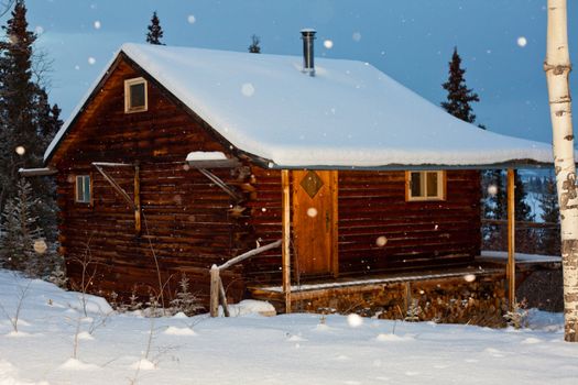 Snowflakes falling on cozy winter cabin inviting you to spend your Christmas holiday.