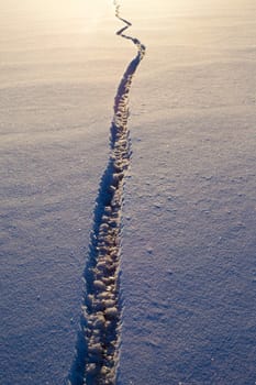 Wide crack in snow-covered ice surface of frozen lake.
