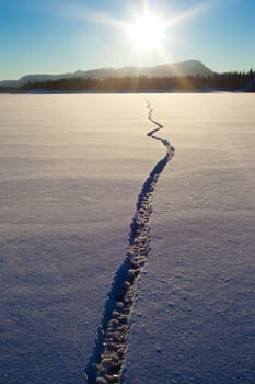 Wide crack in snow-covered ice surface of frozen lake.