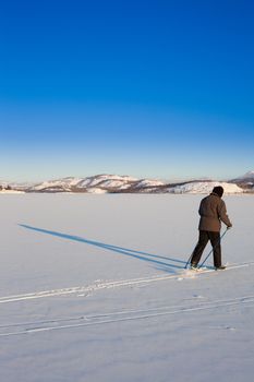 Person skiing on cross-country skis casts long shadow on untouched powder snow.